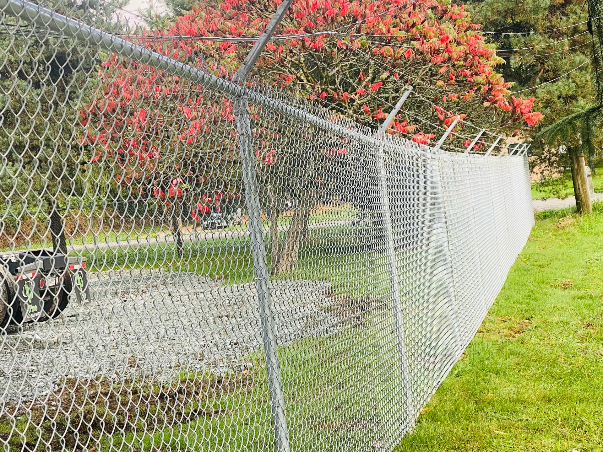 Galvanized chain link fence topped with barbed wire arms along a boulevard