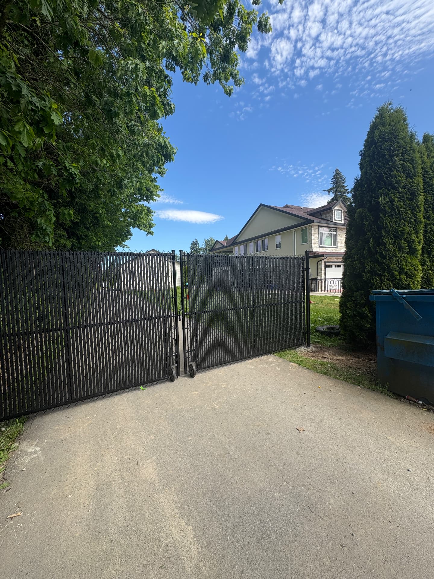 Black chain link double swing gate with privacy slats across a gravel driveway
