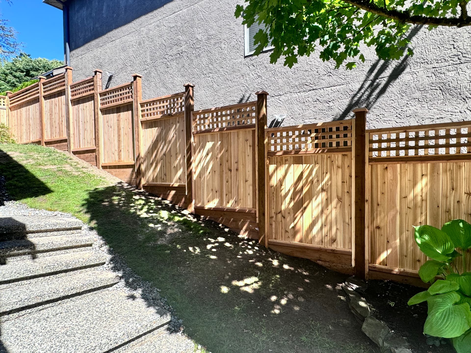 Stepped cedar privacy fence with square lattice top running along a sloped side yard