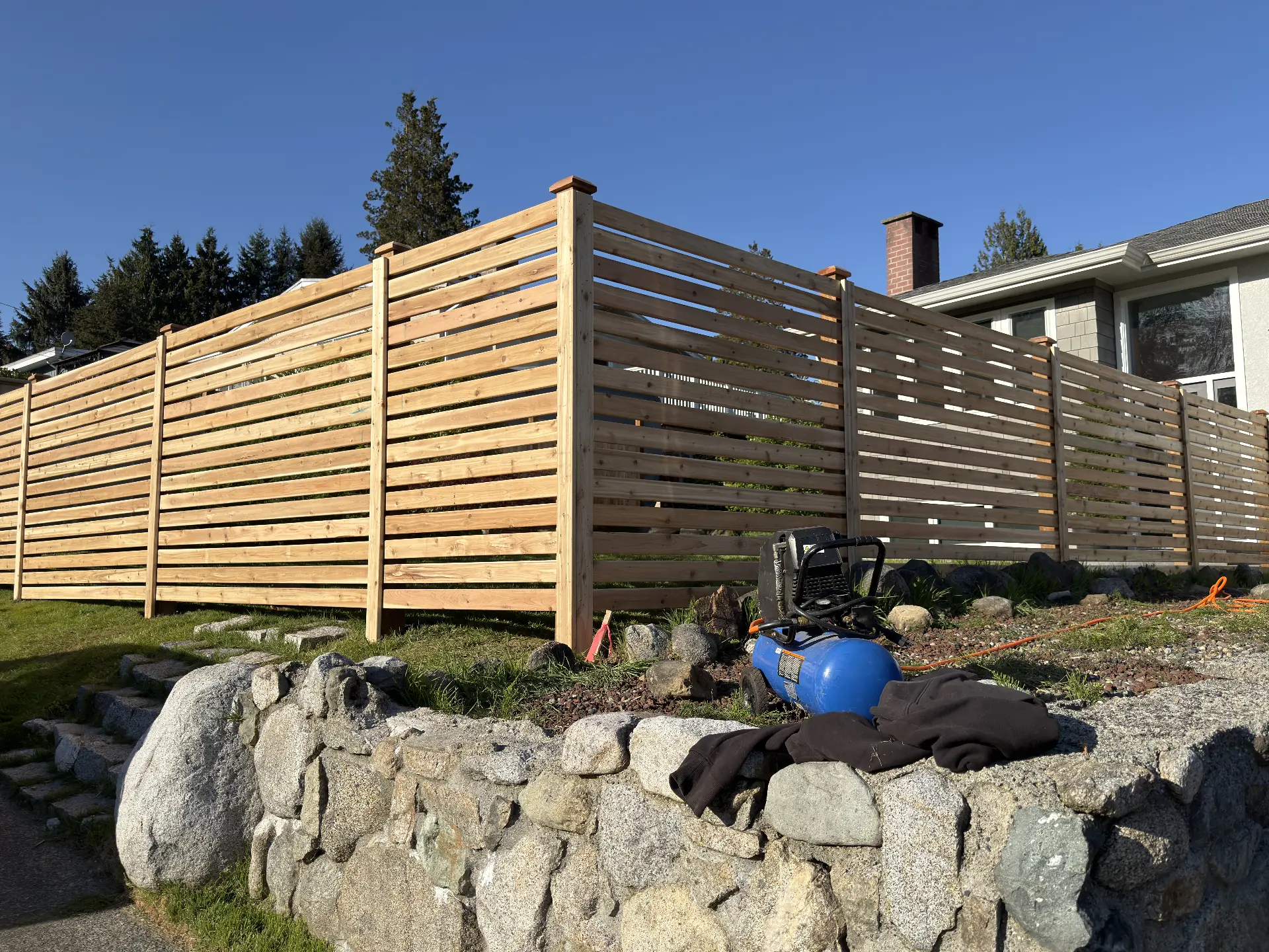 Natural cedar horizontal slat fence with capped posts above a stone retaining wall