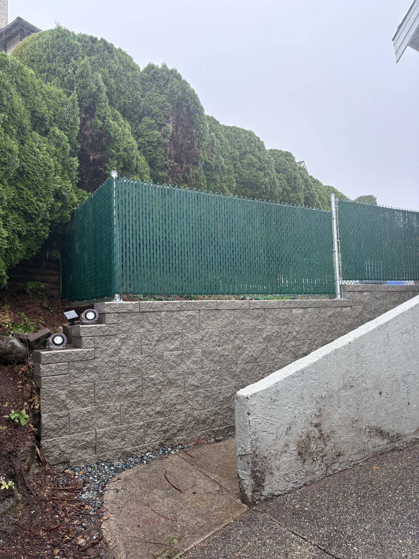 Allan Block retaining wall topped with green privacy slat chain link fence