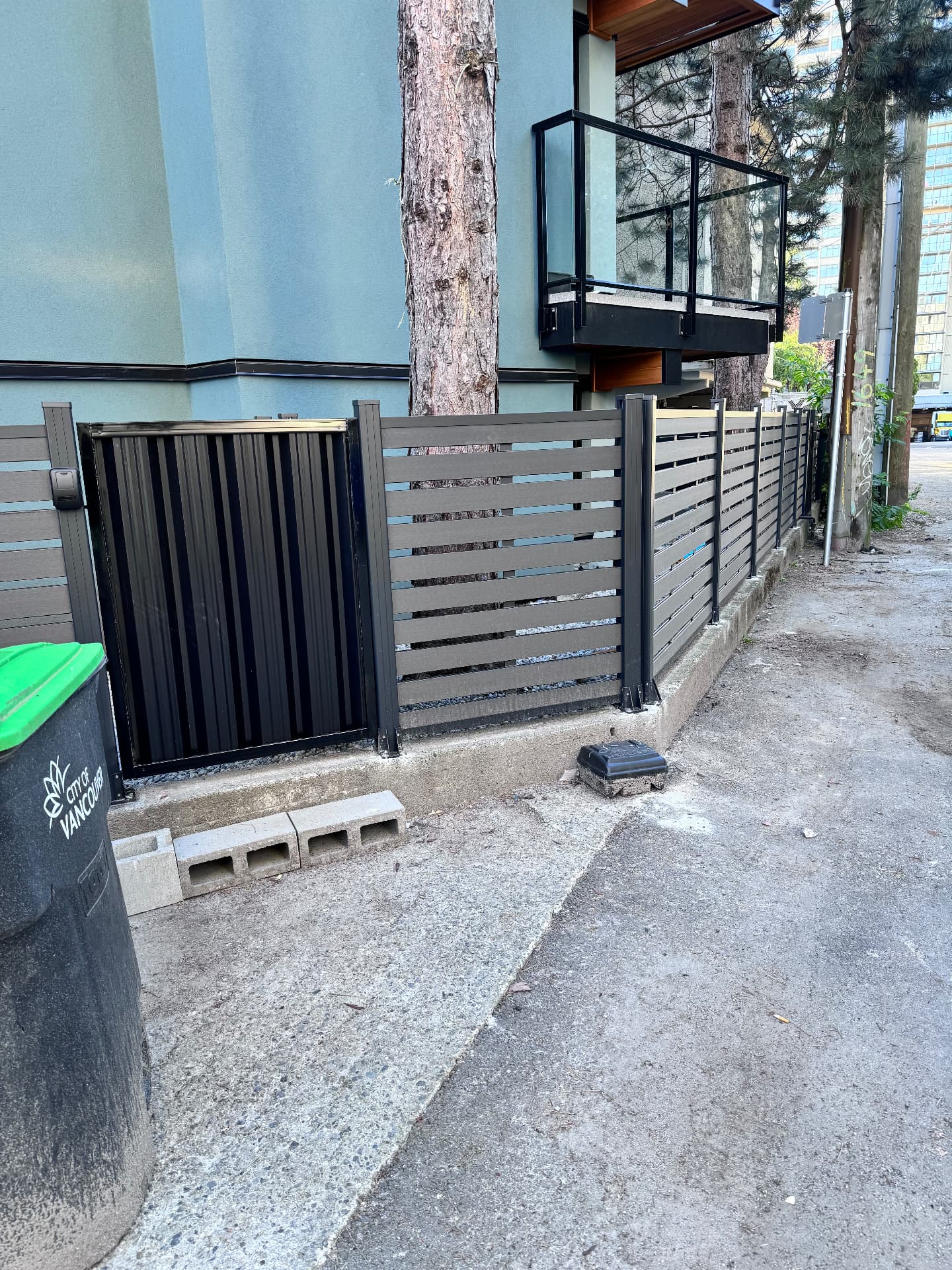 Grey composite slat fence with a black corrugated metal gate beside a building