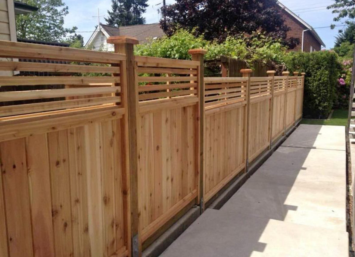 Cedar privacy fence with open spindle top rail and capped posts beside a concrete walkway