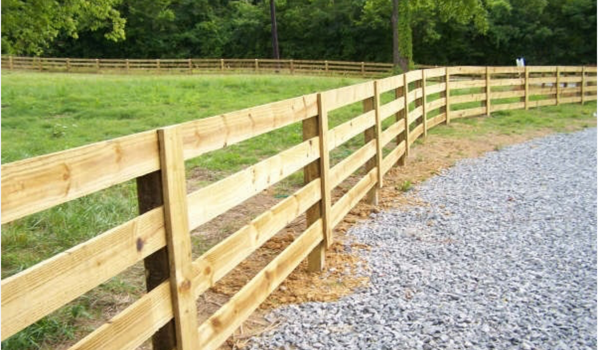 Wood post and rail ranch fence along a pasture and gravel drive
