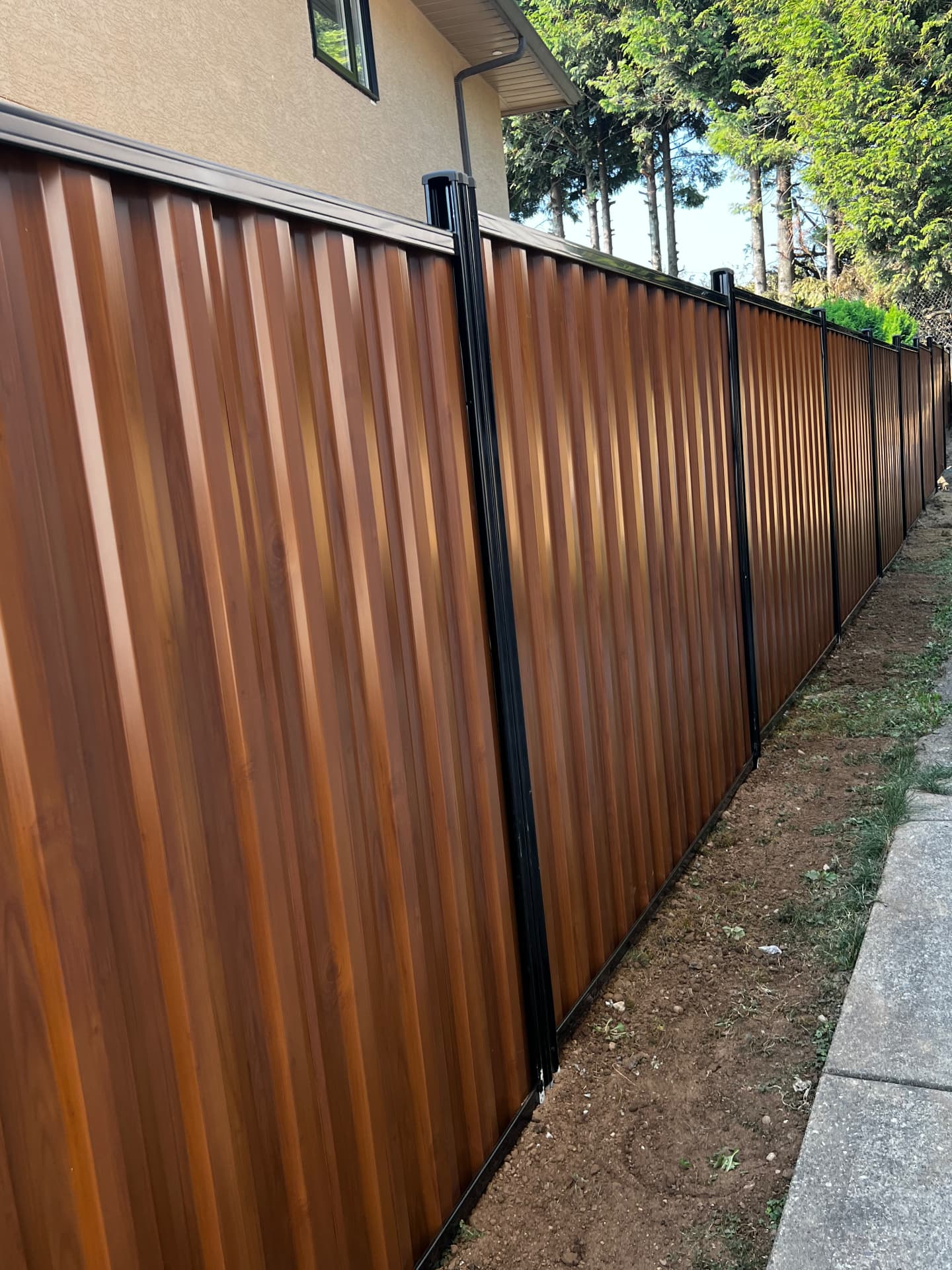 Warm woodgrain corrugated metal privacy fence with black posts along a side yard