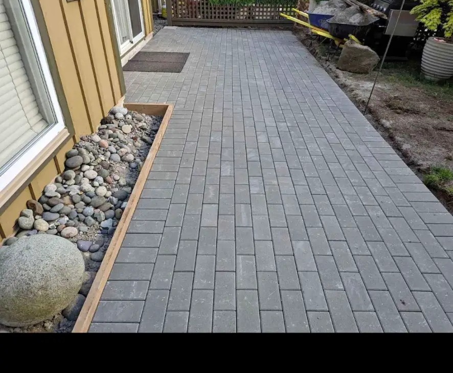Charcoal paving stone walkway beside a house with river rock border