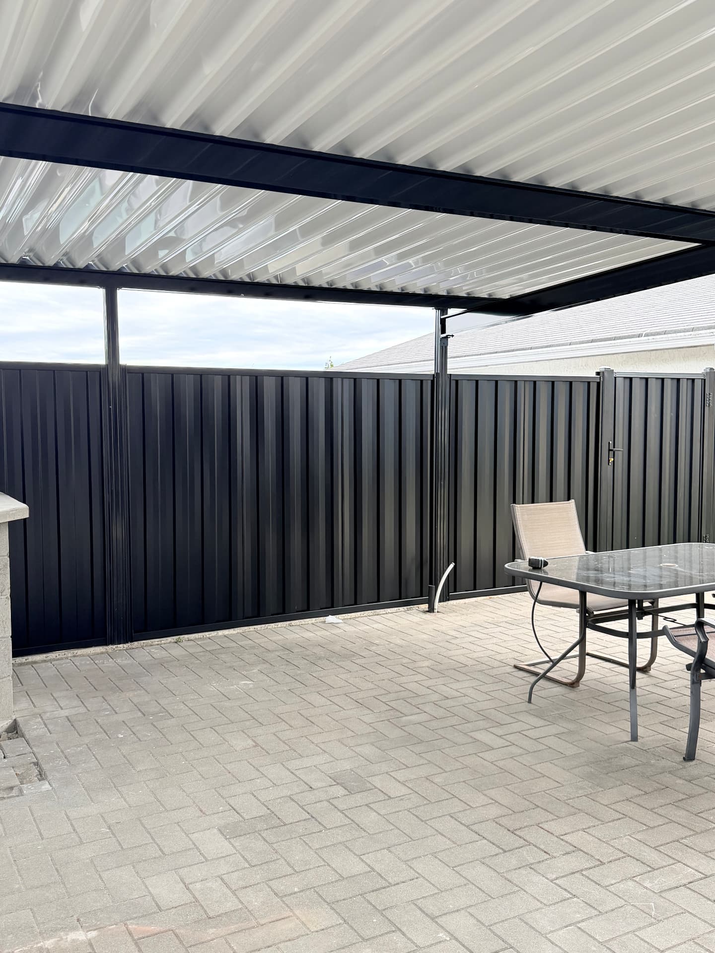Black corrugated metal privacy fence enclosing a covered paver patio