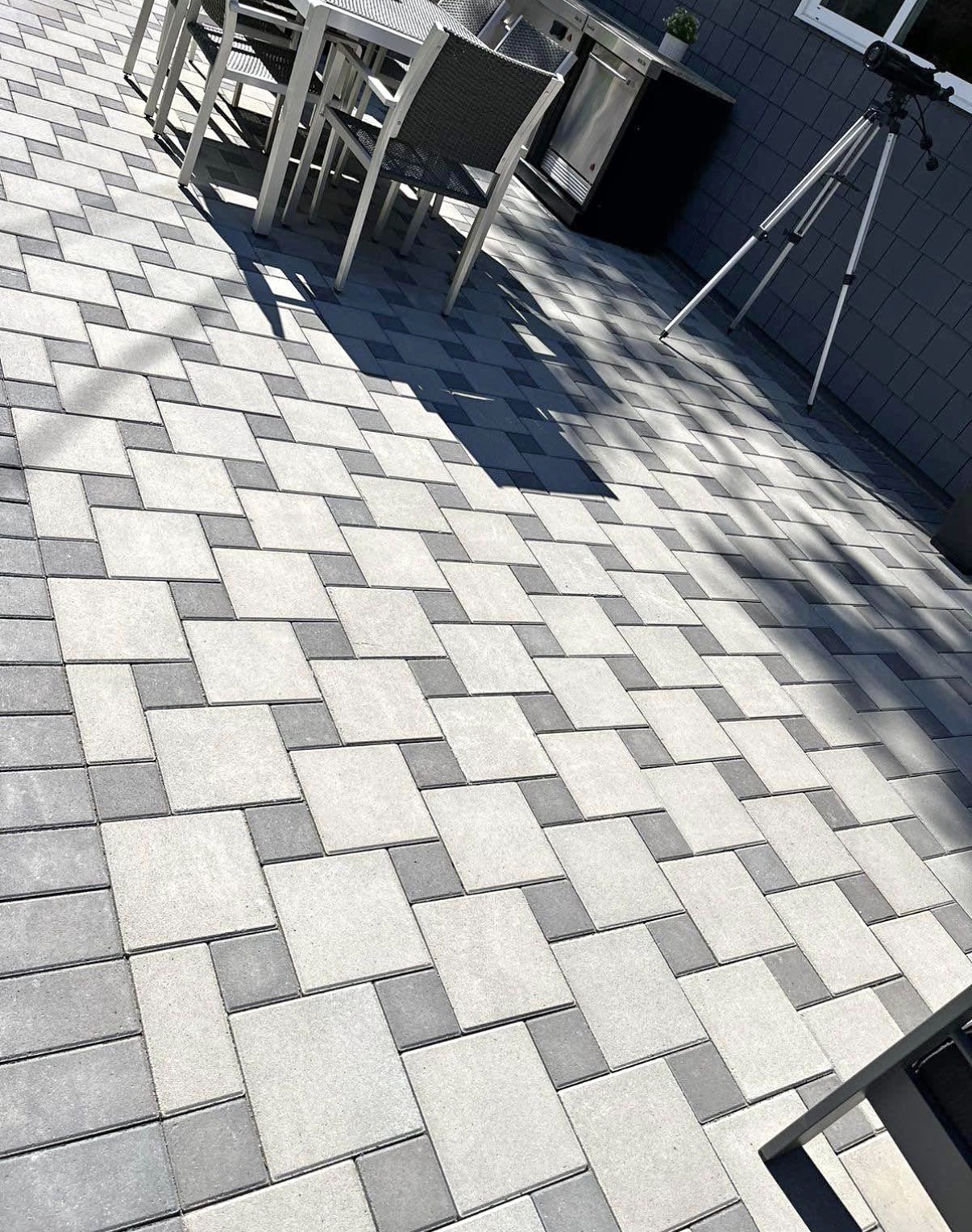 Large grey and white herringbone paver patio with patio furniture beside a modern home