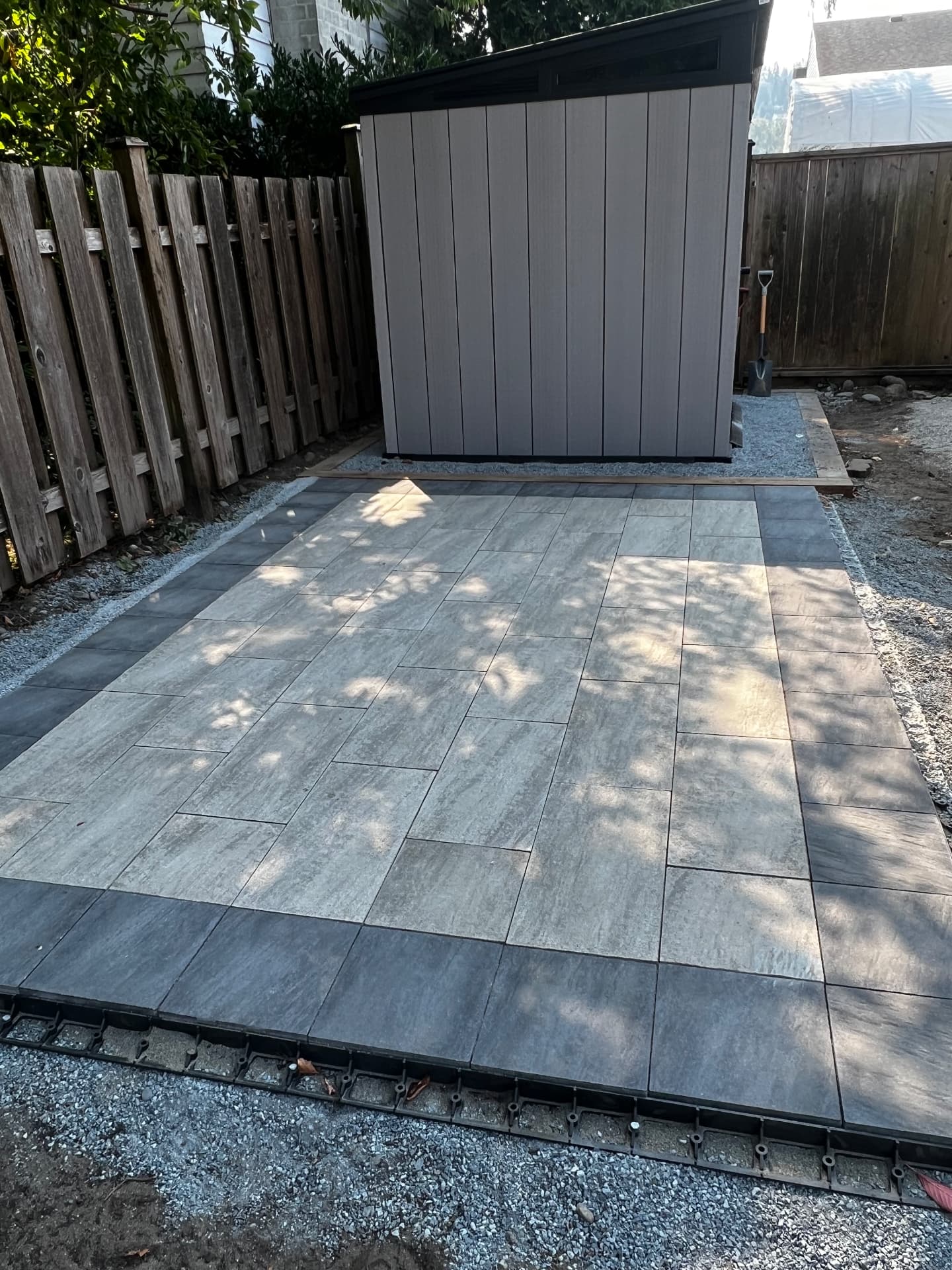 Grey paver patio with charcoal border stones laid for a backyard storage shed