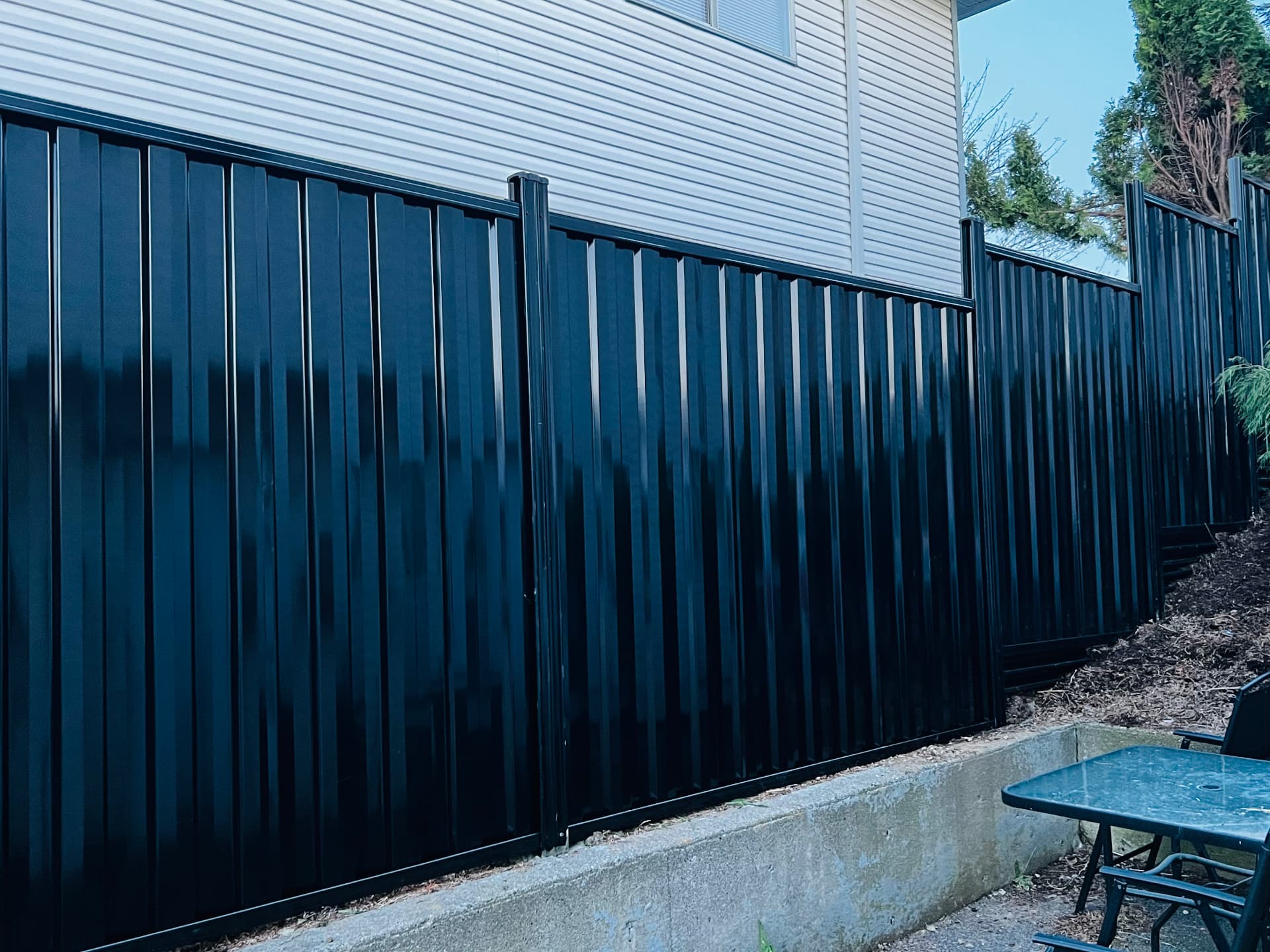 Glossy black corrugated metal privacy fence stepping along a side yard retaining wall