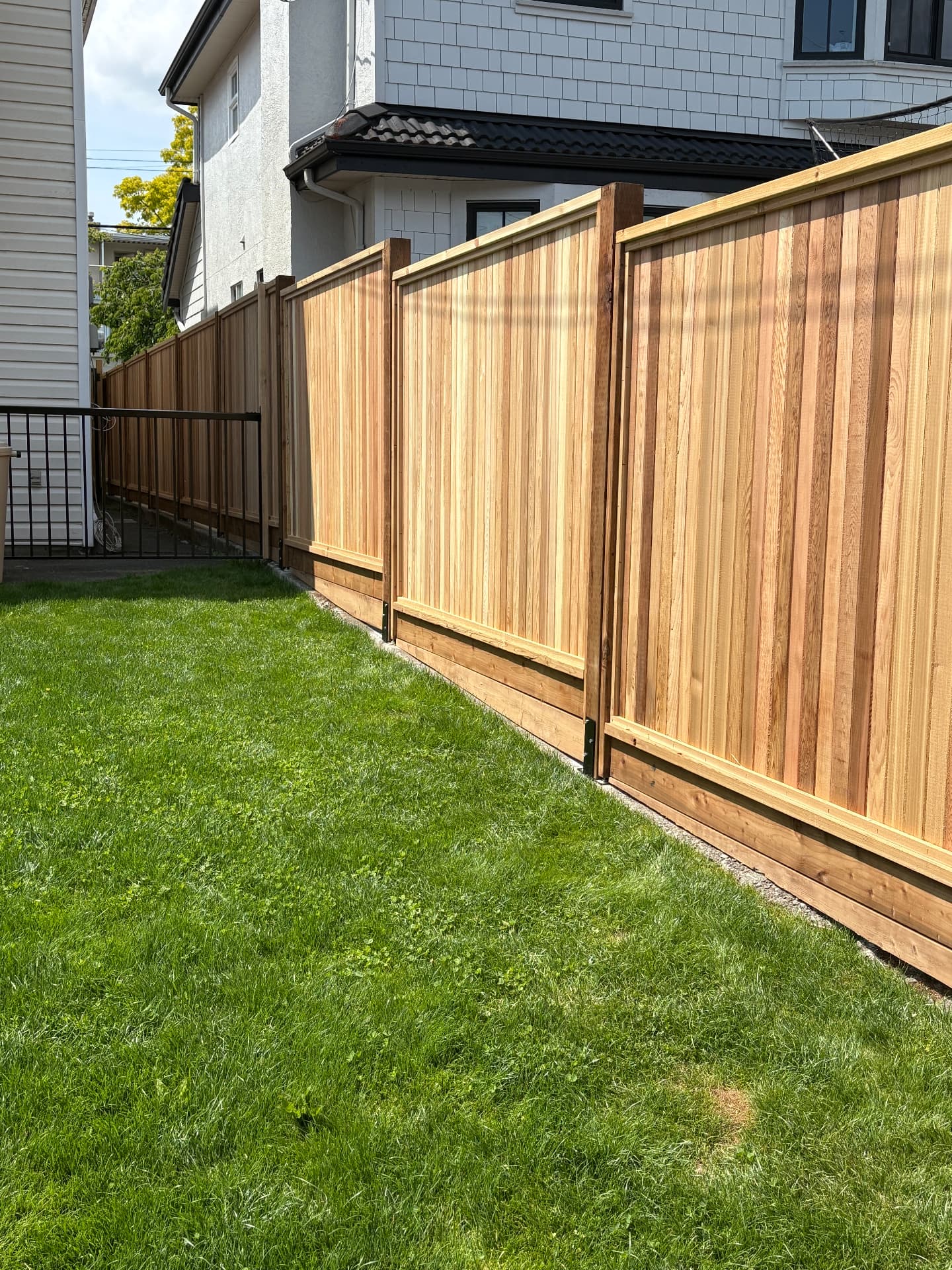 New western red cedar privacy fence with capped top rail along a side yard lawn