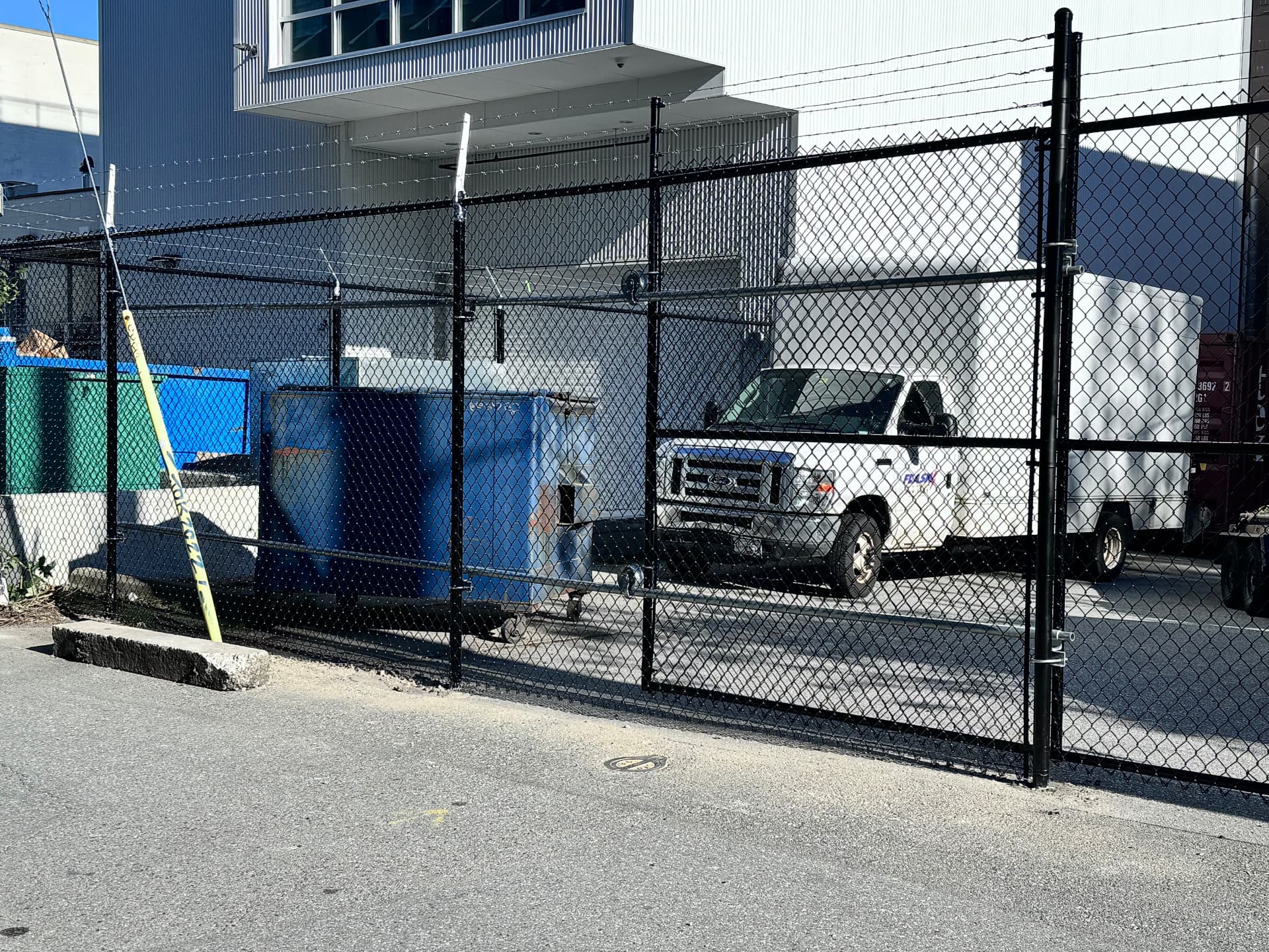 Black chain link commercial double gate topped with barbed wire securing a loading yard