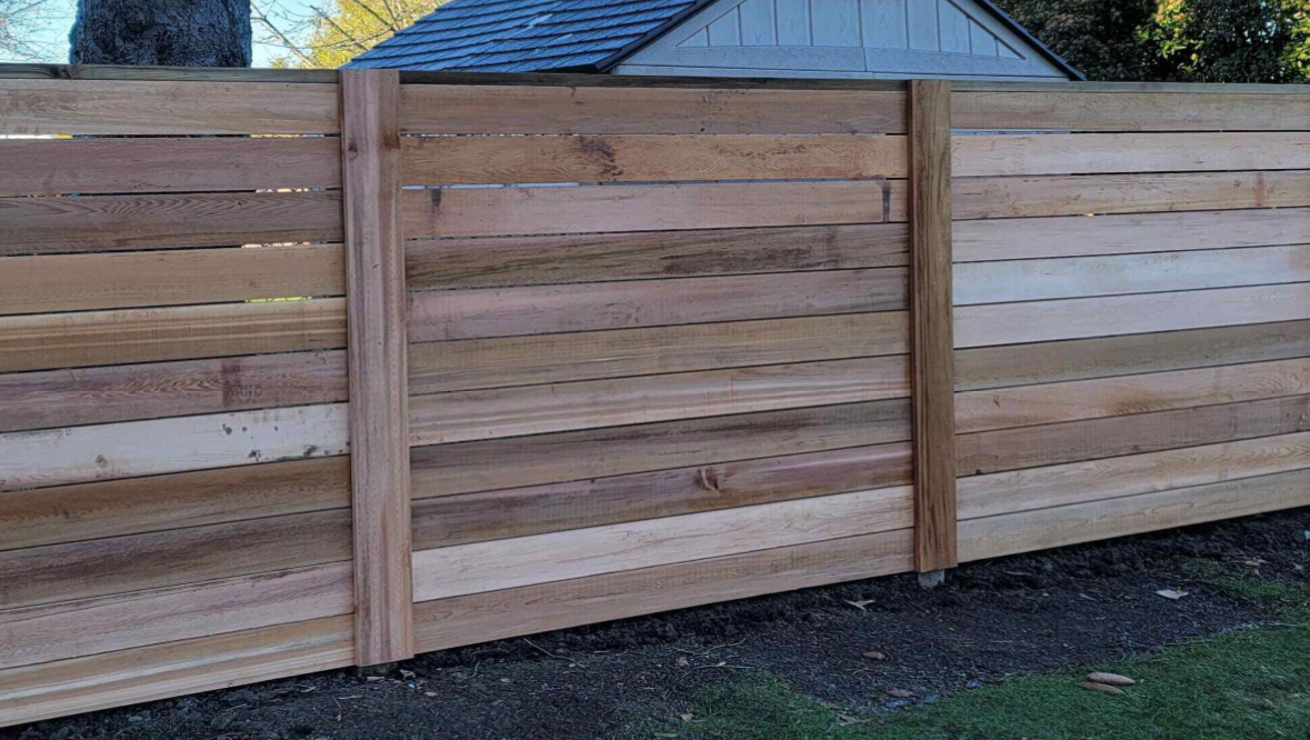 Horizontal cedar board fence with cedar posts along a garden bed