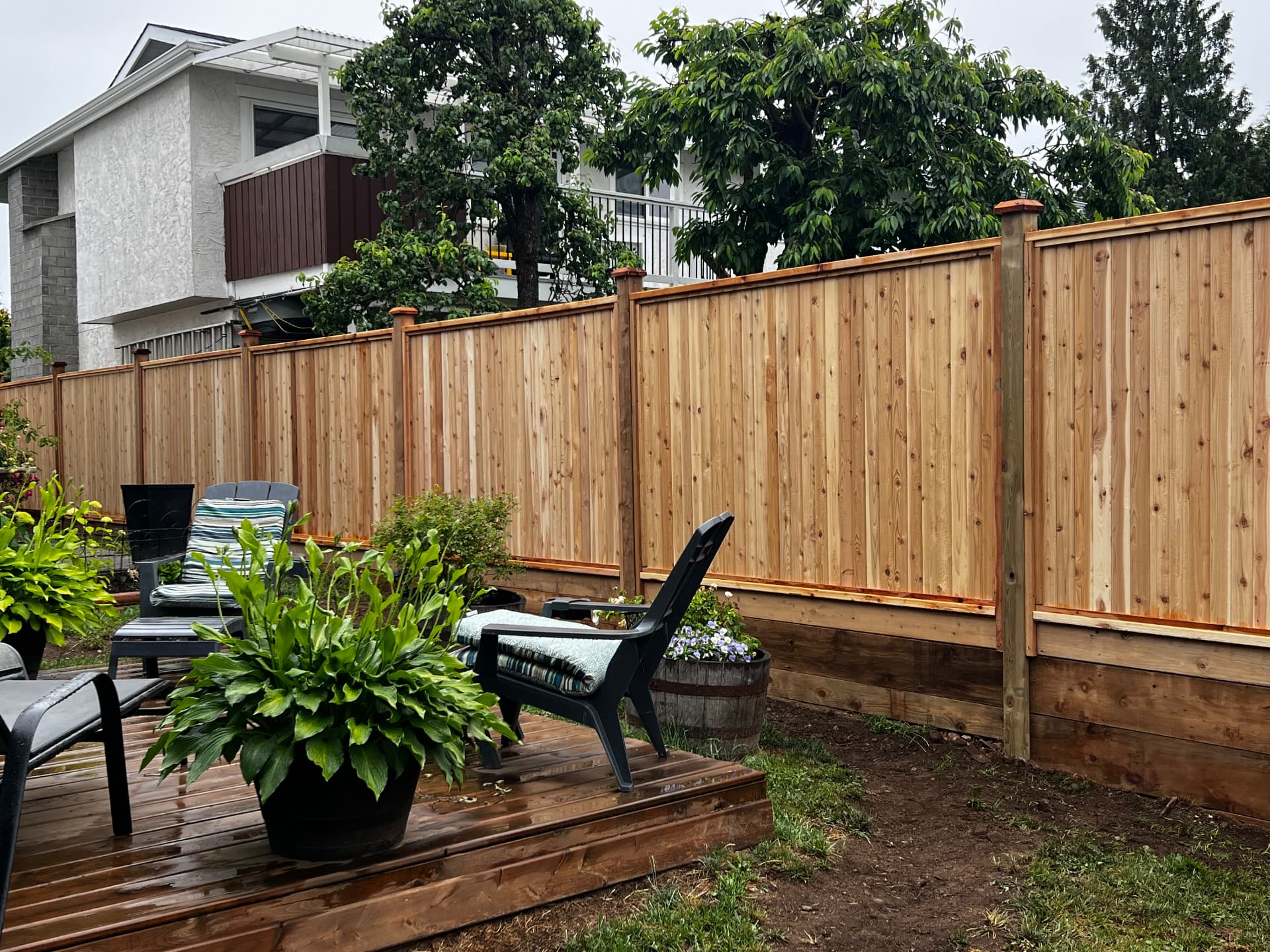 New cedar privacy fence with capped posts beside a low cedar deck and garden seating
