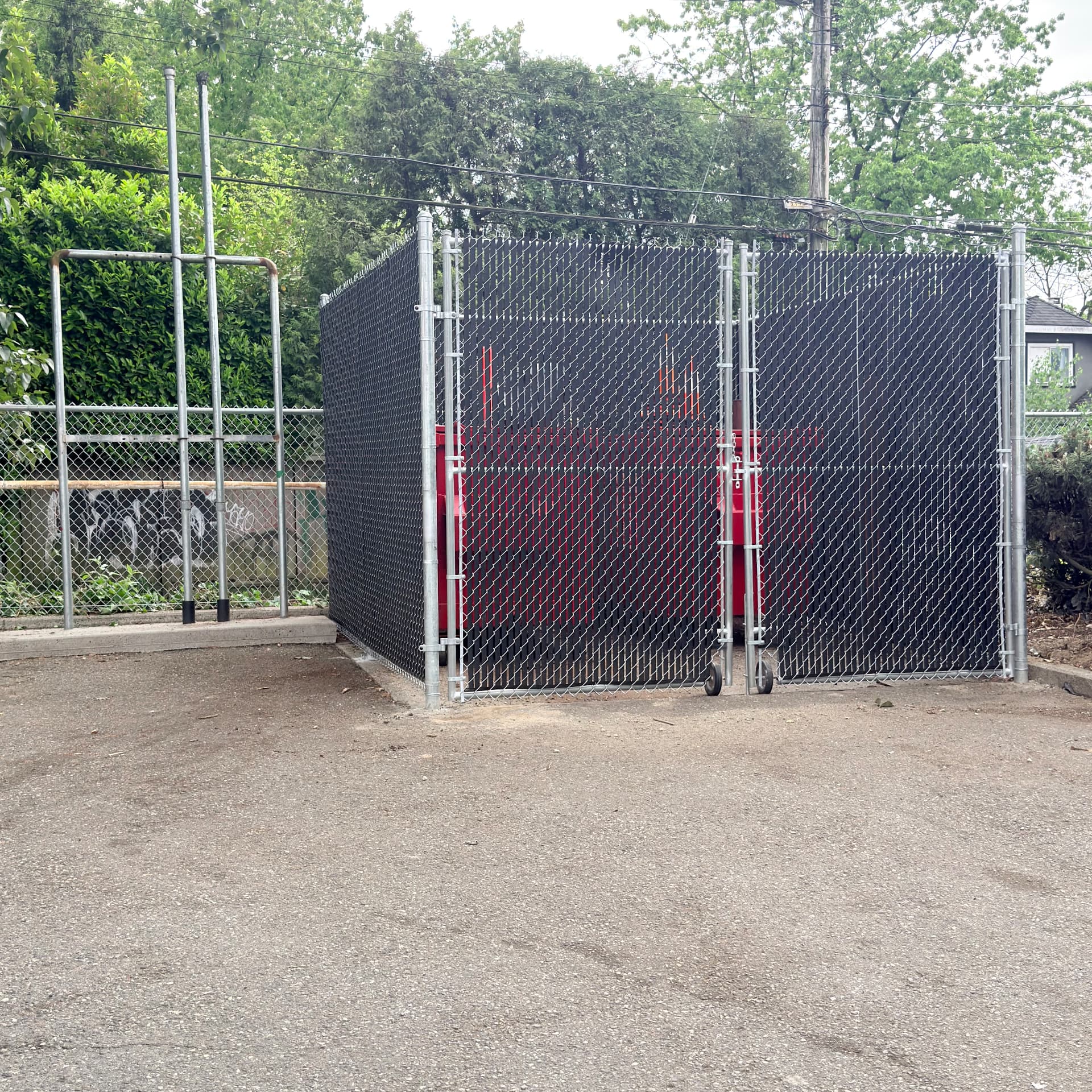 Galvanized chain link garbage enclosure with black privacy slats and rolling gates
