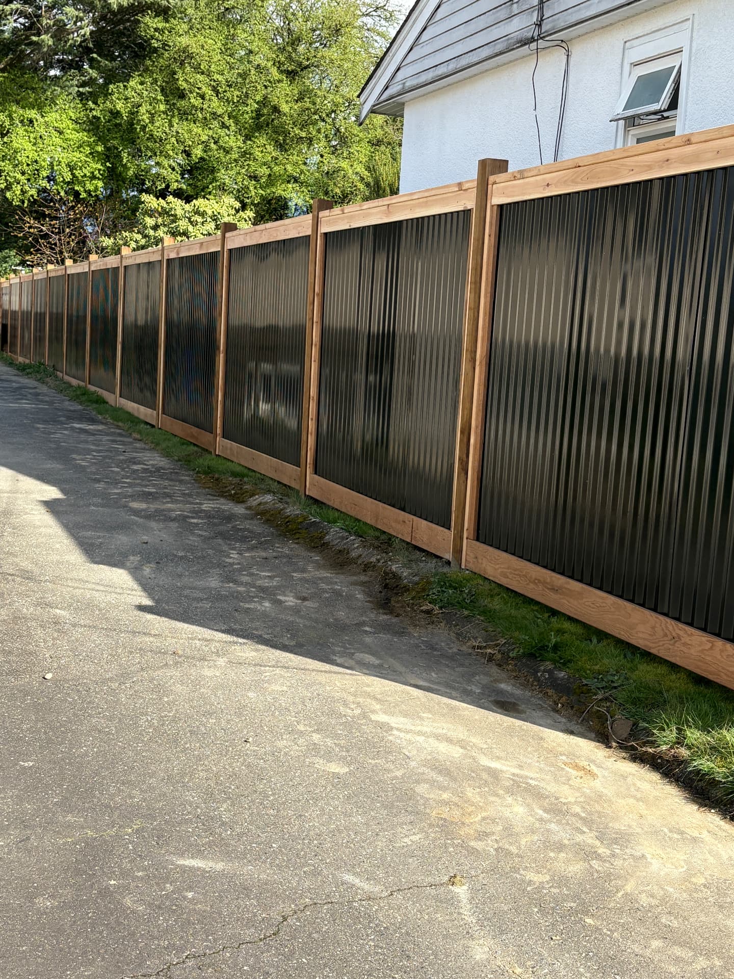 Black corrugated metal privacy fence framed in cedar along a lane
