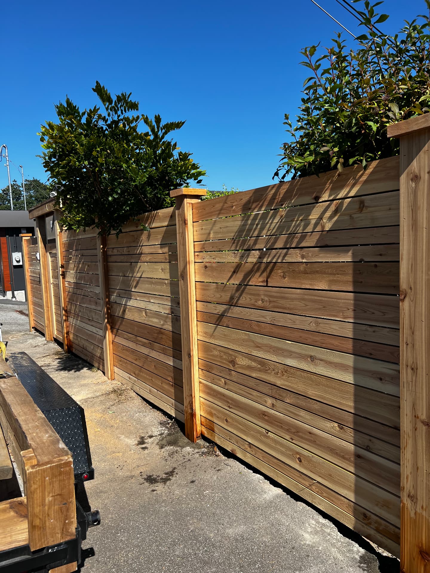 Horizontal cedar slat fence with capped posts running along a paved laneway