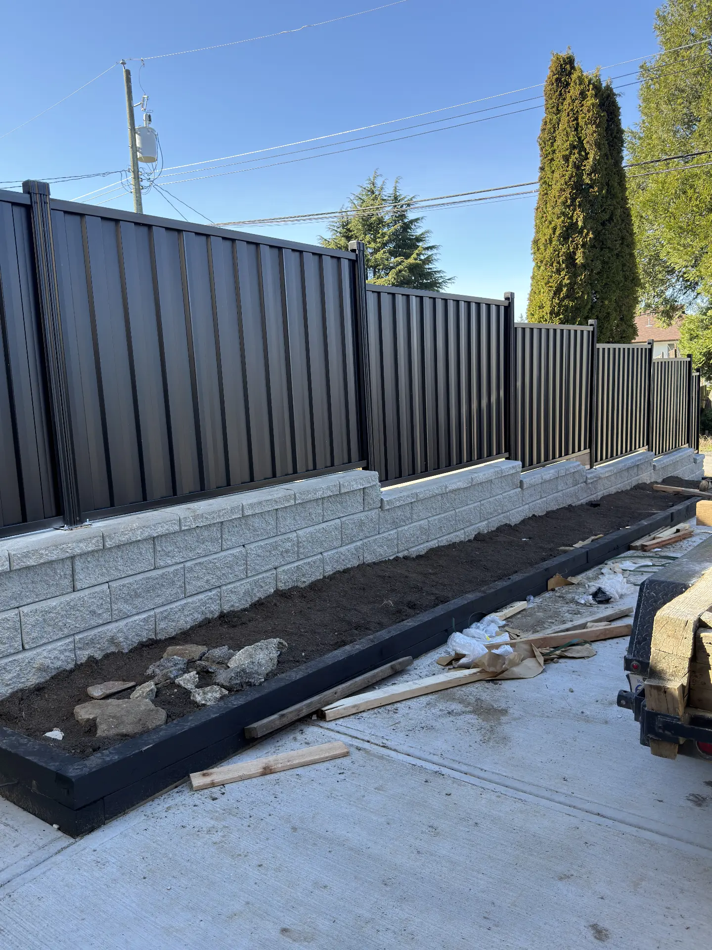 Black metal privacy fence panels mounted on a grey Allan Block retaining wall