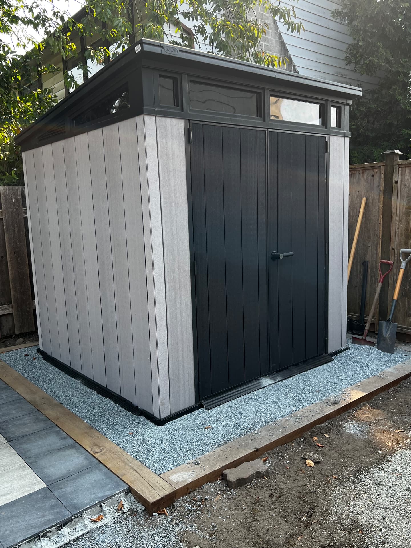 Backyard shed set on a compacted gravel pad with timber edging next to a paver patio