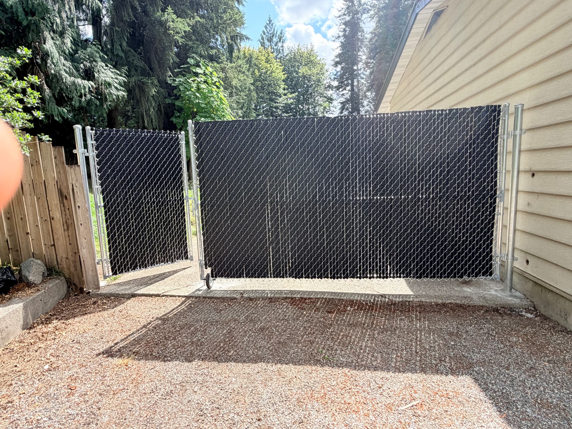 Galvanized chain link rolling gate filled with black privacy slats beside a house