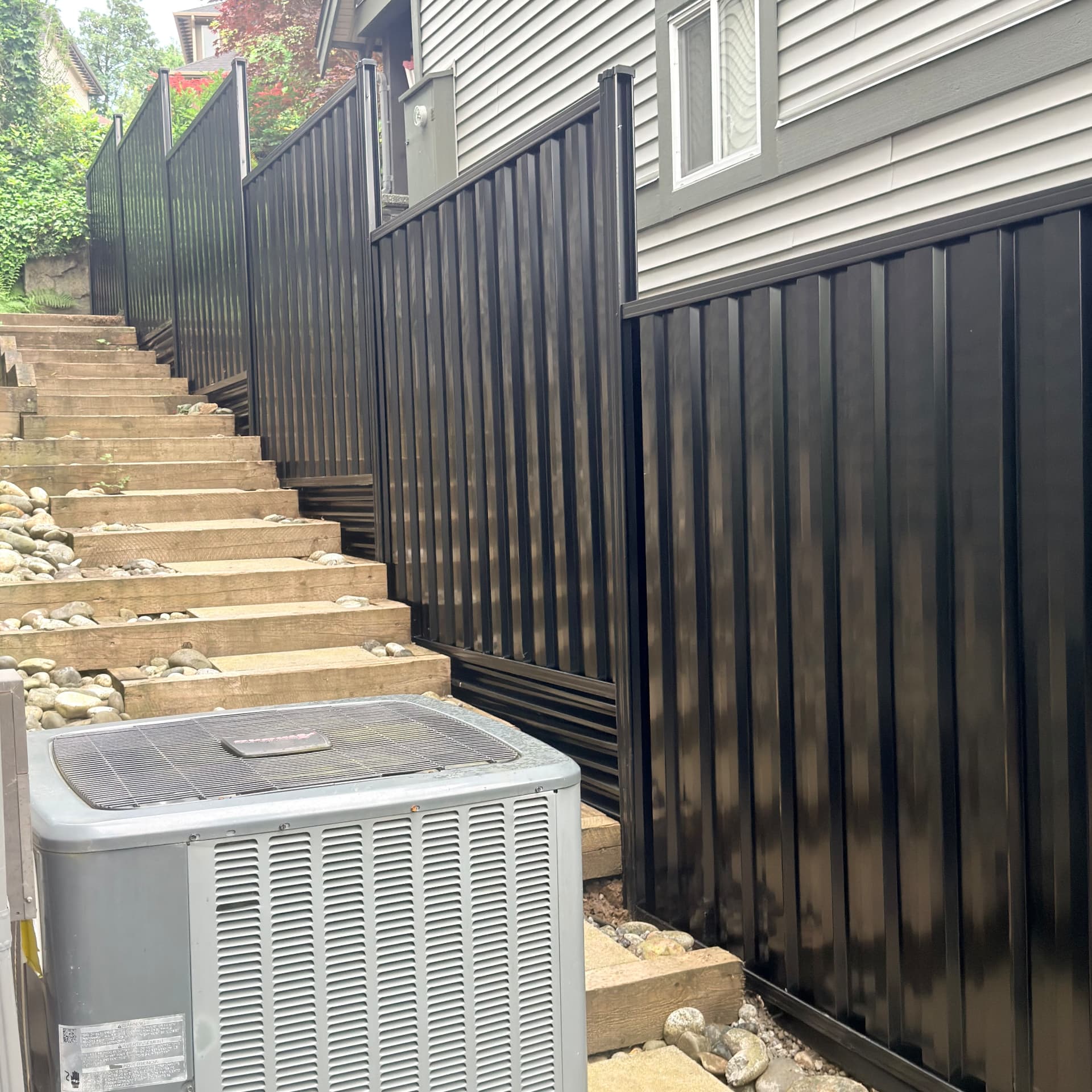 Black metal privacy fence stepping down a sloped side yard beside timber stairs