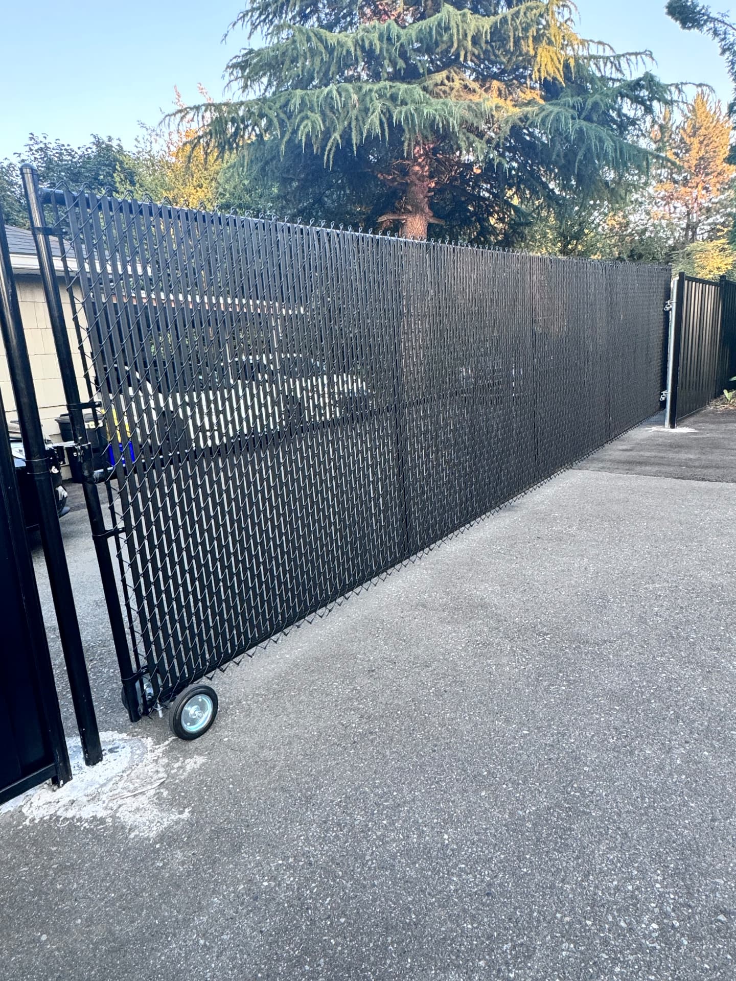 Black chain link rolling driveway gate with privacy slats on a wheel track