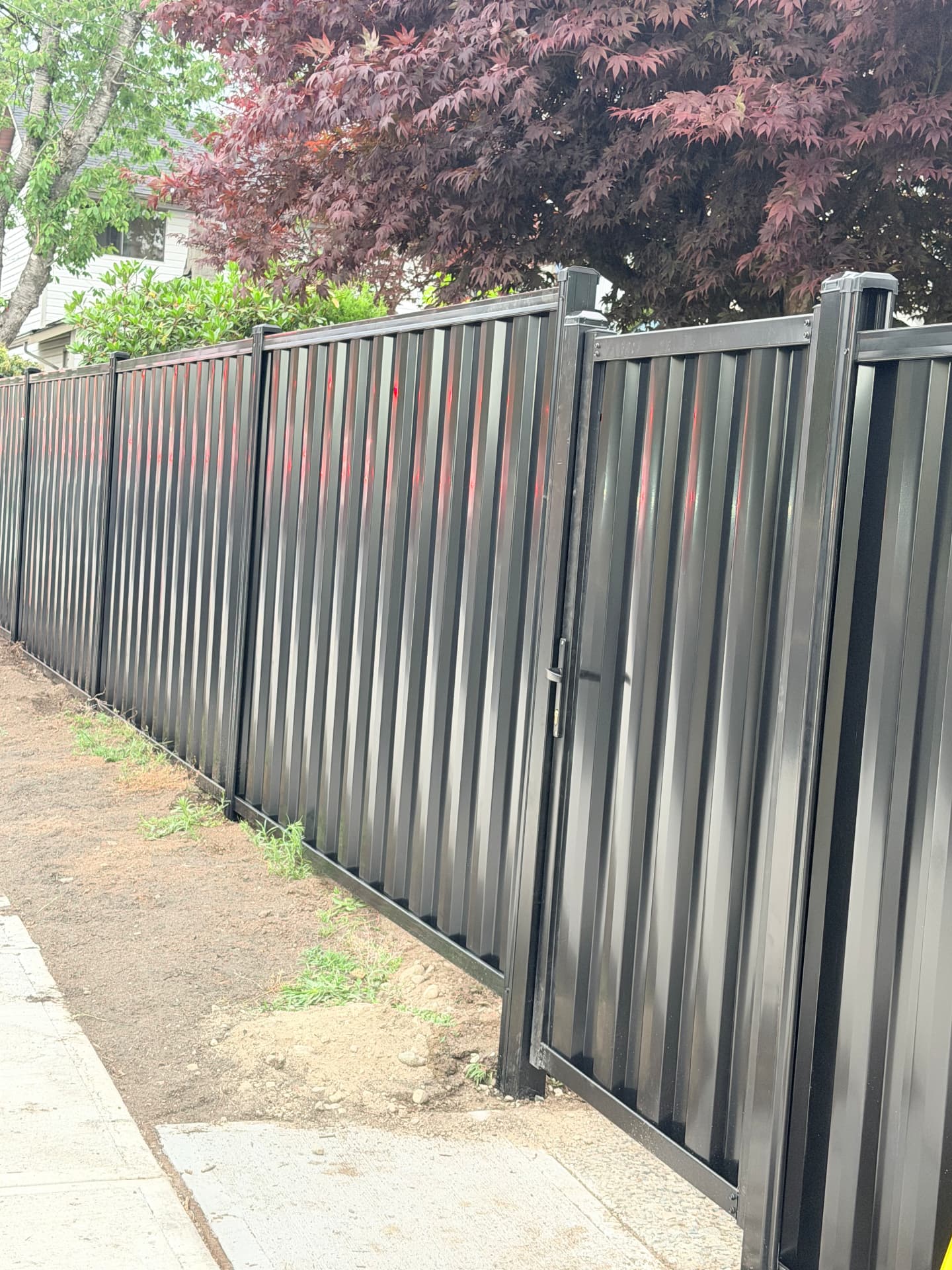 Black metal privacy fence with matching gate running along a city sidewalk