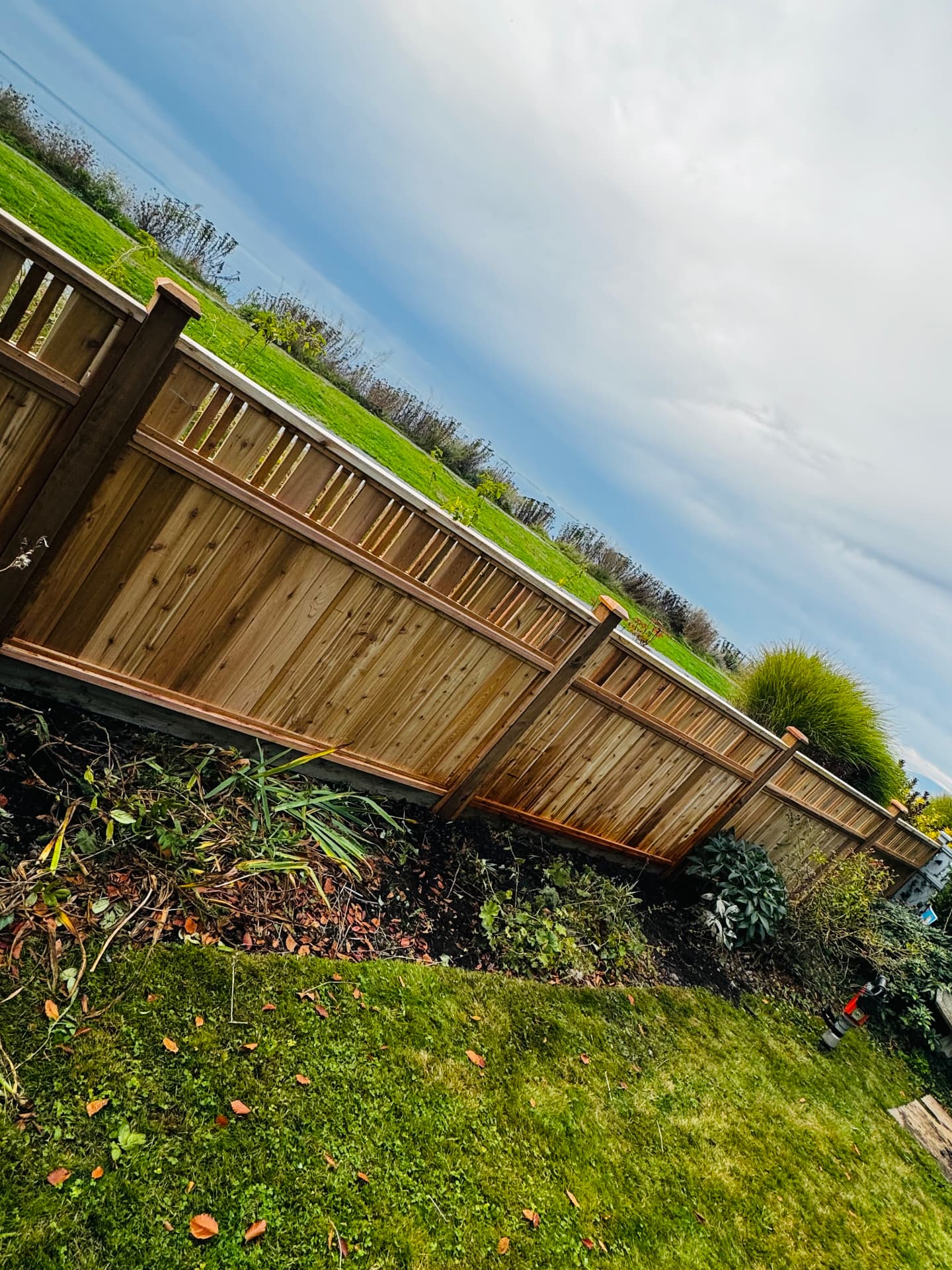 Cedar privacy fence with spindle top rail and capped posts running along a landscaped lawn