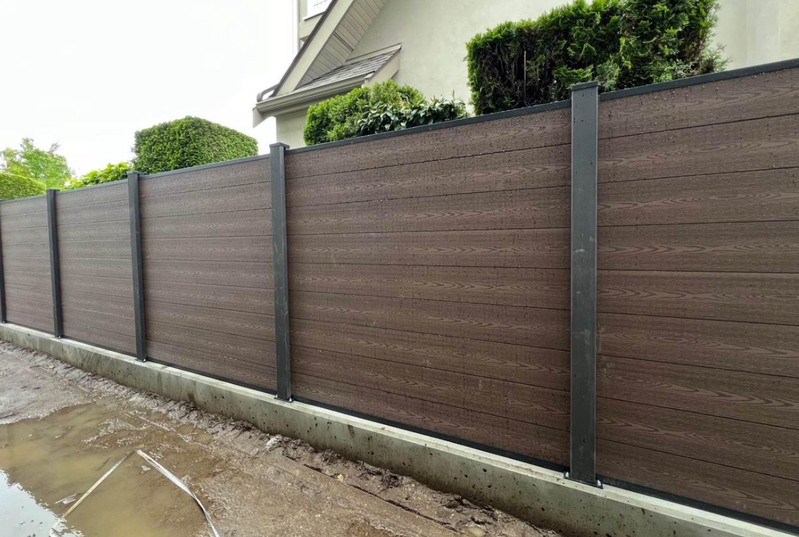 Brown woodgrain composite fence panels with black aluminum posts on a concrete curb