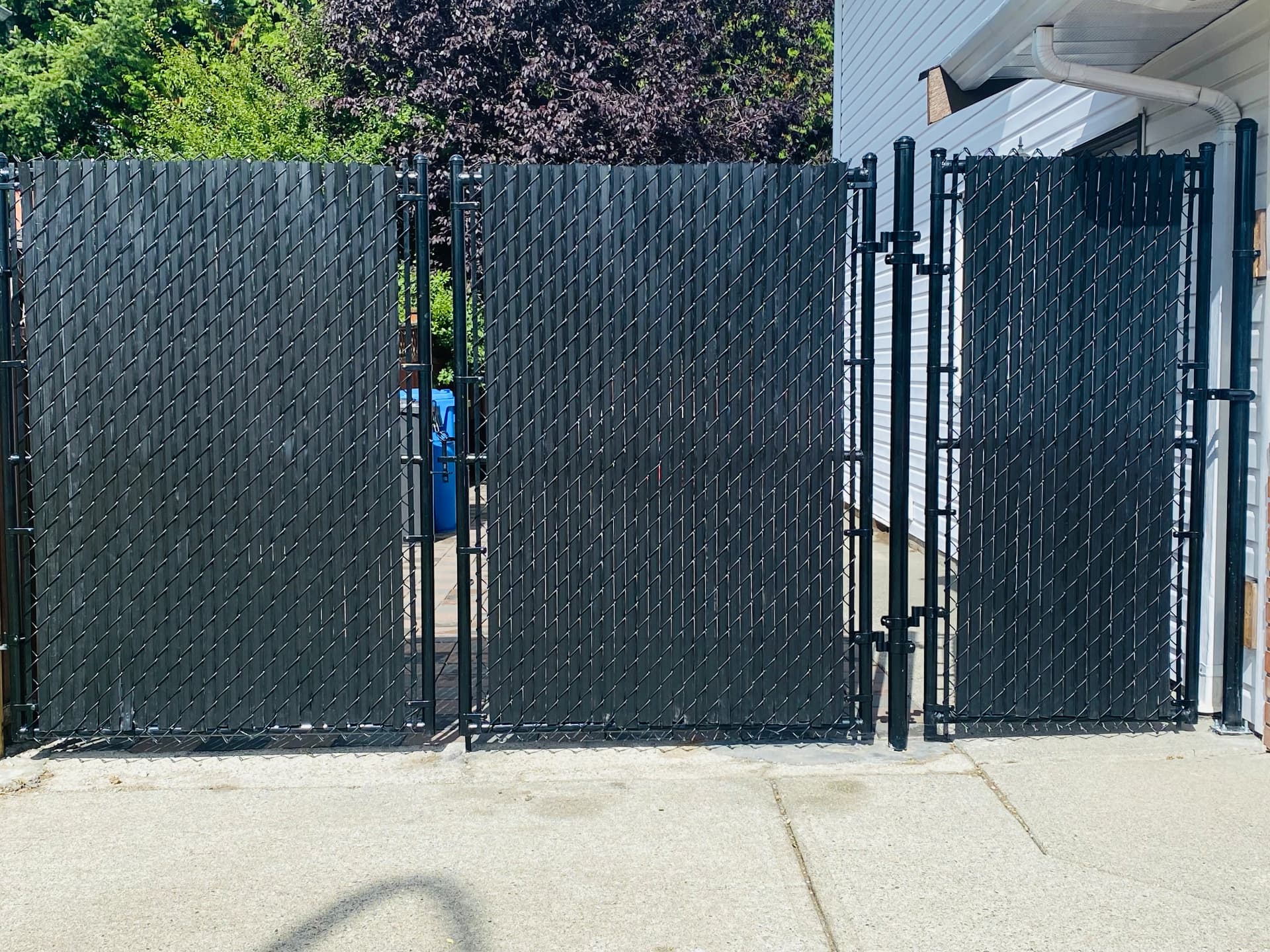 Black chain link privacy gates with woven slats screening a garbage enclosure
