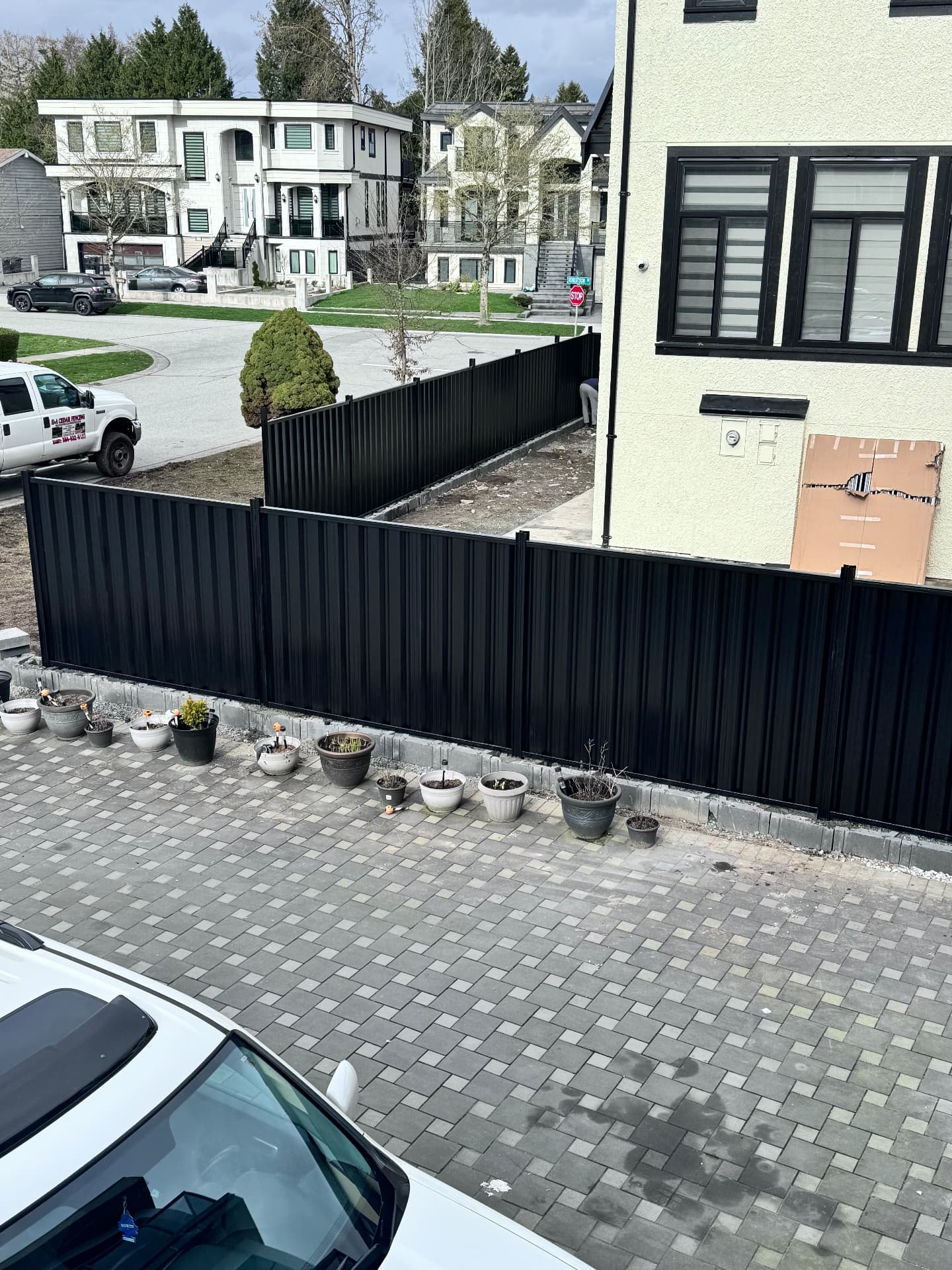 Black corrugated metal fence wrapping a corner lot above a paver driveway