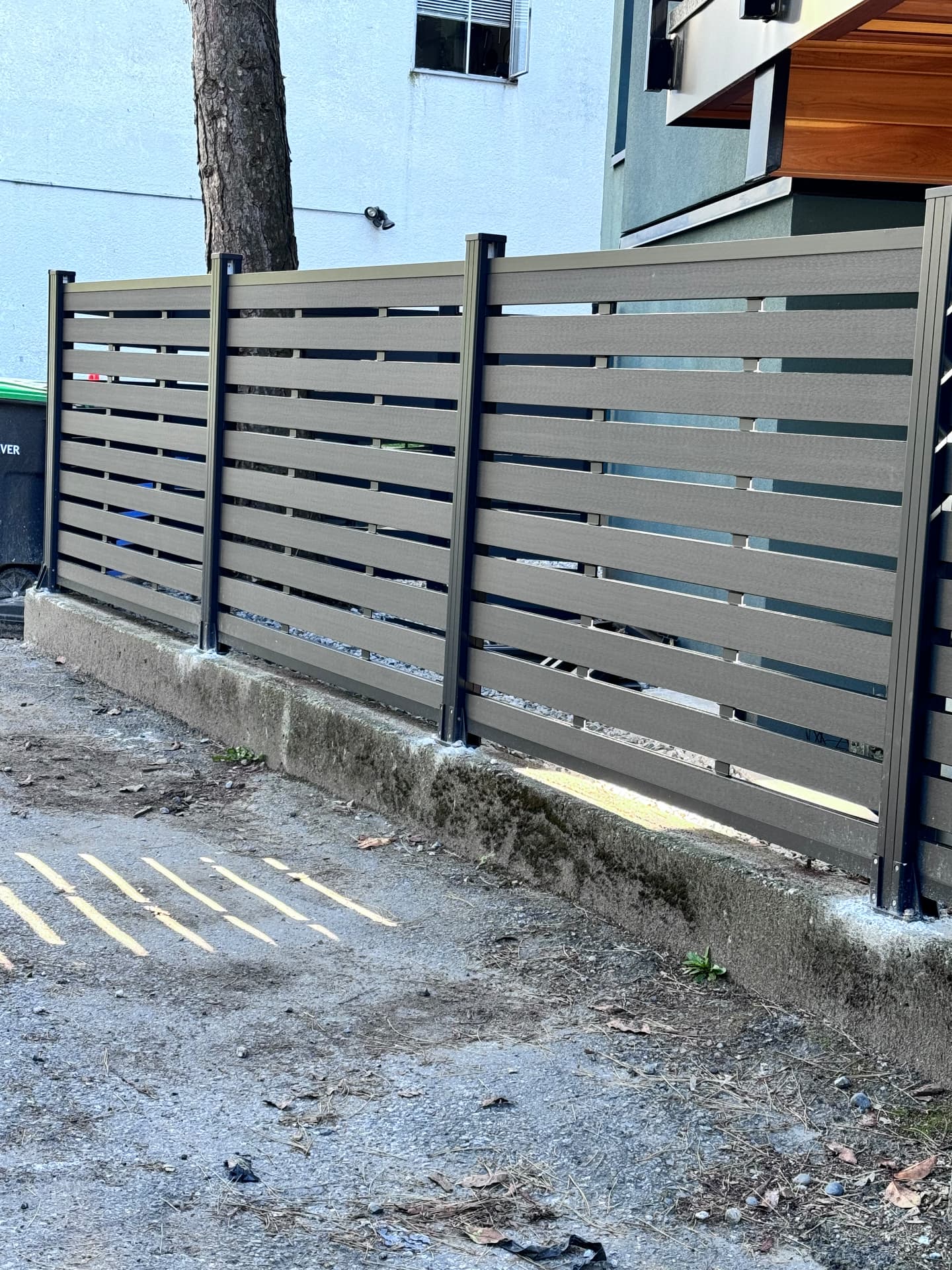 Grey horizontal composite slat fence with black aluminum posts along a laneway