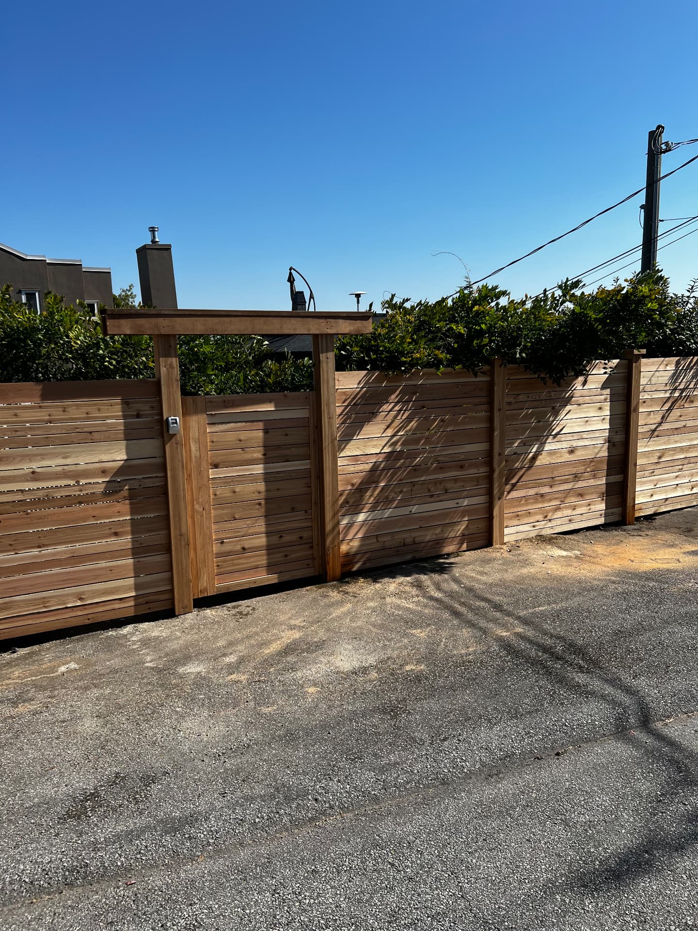 Horizontal cedar slat fence with a pergola-topped keypad gate off a laneway