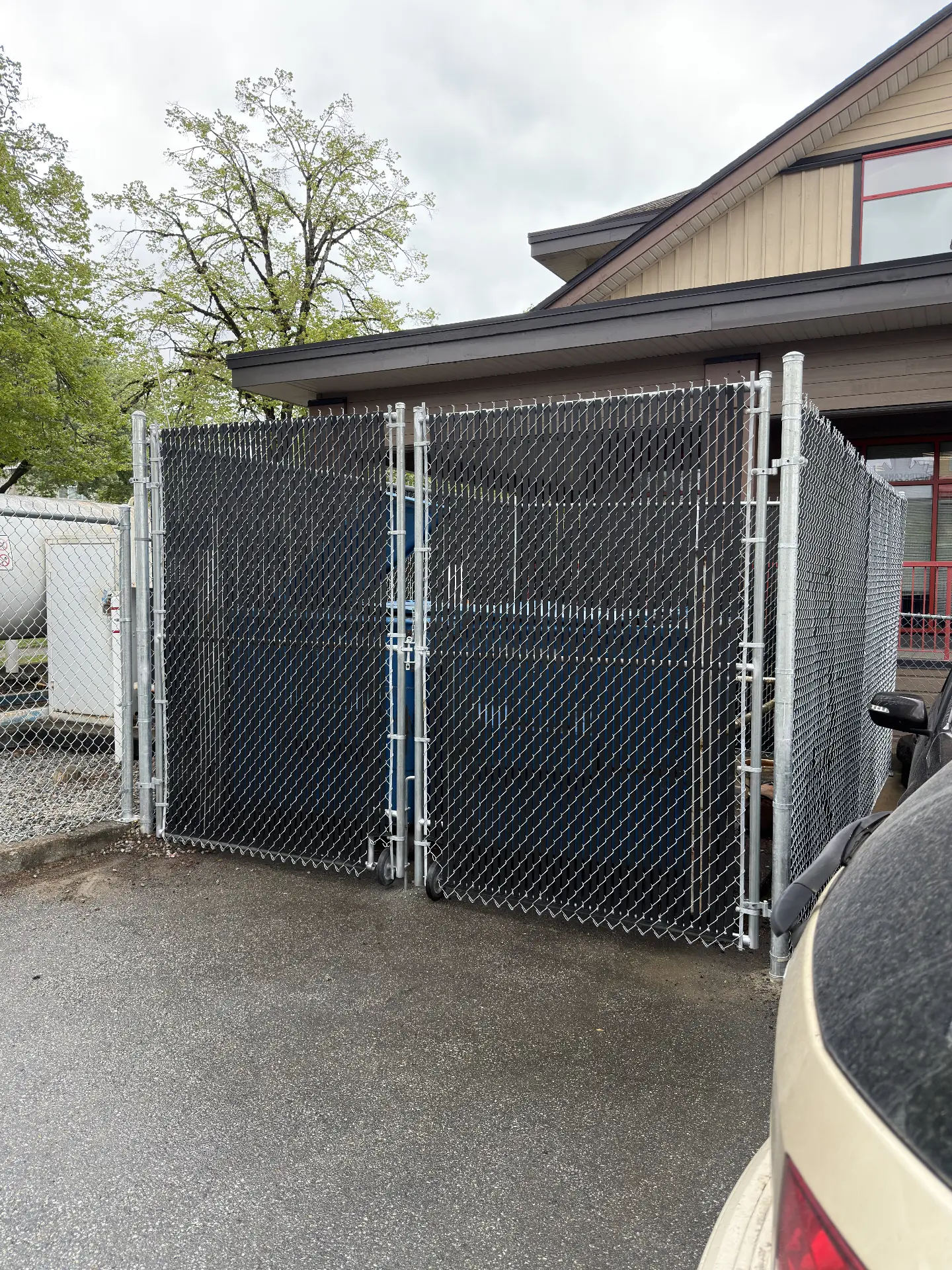 Chain link dumpster enclosure with black privacy slats and double rolling gates