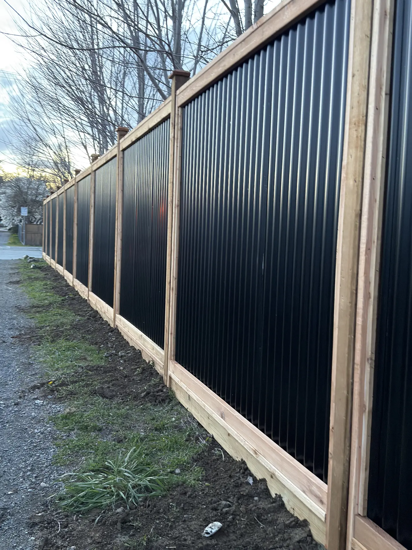 Long black corrugated metal fence framed in natural cedar posts and rails along a lane